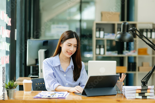 Young Asian woman, smiling and working at her desk in an office environment.