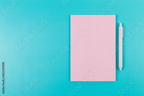 Top view of pink notebook, pink pen on blue background. School, office wallpaper. Flat lay, copy space.