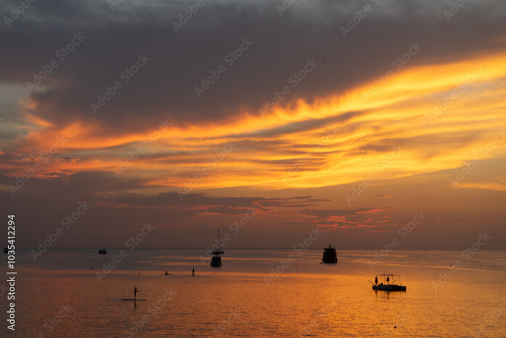 A serene sunset over calm waters with silhouetted boats. A serene sunset over calm waters with silhouetted boats.