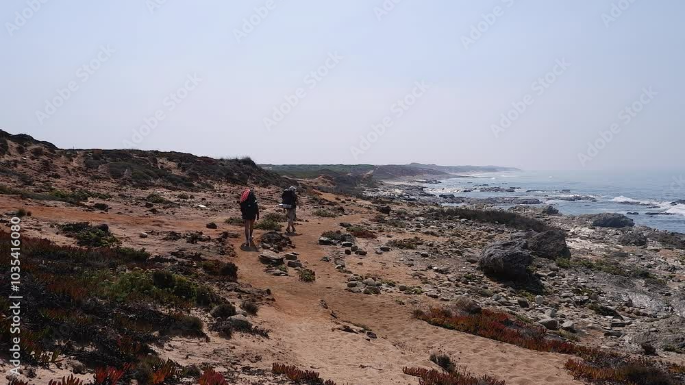 Two young backpackers hike rugged ocean coastline, endless blue sky Two young backpackers hike rugged ocean coastline, endless blue sky