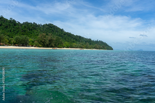 A serene view of a tropical beach with clear blue waters and lush green hills.