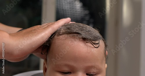 Hand placed gently over baby’s wet hair during bath, calming the baby, intimate bath care, baby with water droplets on head, relaxing bath care moment. 800 fps slow-motion photo