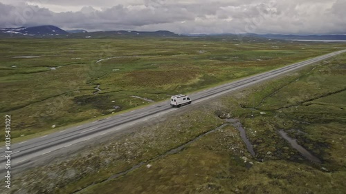 Aerial view of a winding wilderness road with a camper van surrounded by serene greenery and expansive landscape, Stromsund, Sweden.