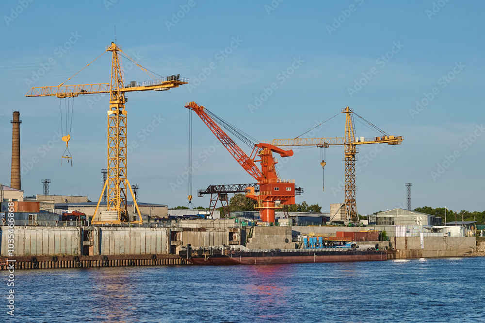 Obraz premium Port cranes on the pier of the commercial port on a summer evening. Bright colors in the rays of the setting sun. The border river Amur between Russia and China.