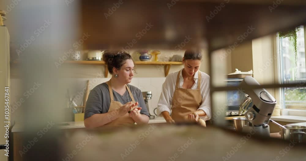 Side view of two girls bakers in beige aprons making spheres from green dough while preparing desserts in a cafe Side view of two girls bakers in beige aprons making spheres from green dough while preparing desserts in a cafe