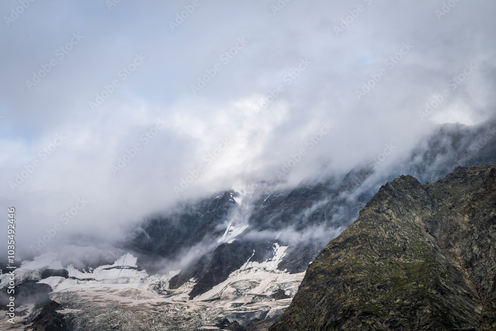 View of majestic snow-covered peaks and clouds in the serene saas valley, valais, switzerland. View of majestic snow-covered peaks and clouds in the serene saas valley, valais, switzerland.