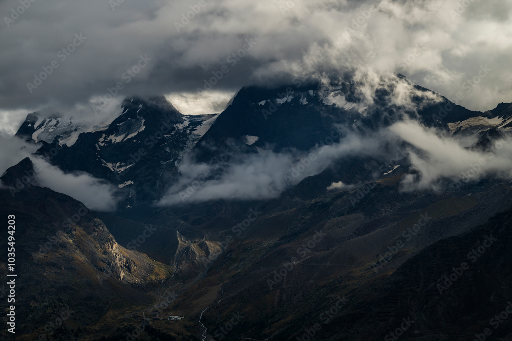 View of majestic mountains and a serene valley shrouded in clouds, Saas Fee, Switzerland. View of majestic mountains and a serene valley shrouded in clouds, Saas Fee, Switzerland.