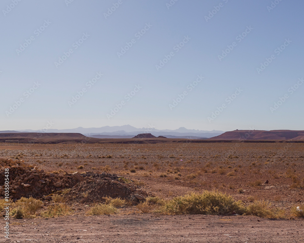 View of vast arid desert landscape with rugged terrain under a clear sky, Draa-Tafilalet, Morocco. View of vast arid desert landscape with rugged terrain under a clear sky, Draa-Tafilalet, Morocco.