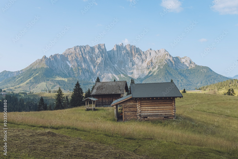 View of mountain huts in the Latermar Mountains with serene grassland and rustic wooden cabins, Nova Levante, Italy. View of mountain huts in the Latermar Mountains with serene grassland and rustic wooden cabins, Nova Levante, Italy.