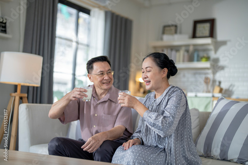An elderly couple enjoys a peaceful moment at home, sharing smiles and drinks. The warm and cozy atmosphere emphasizes their deep connection, happiness, and the comfort of spending time together.