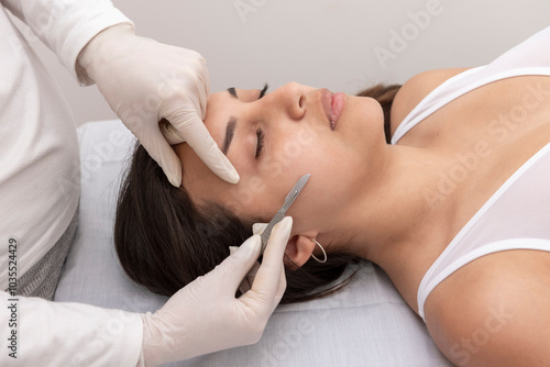 young woman on a table in a beauty center performing a beauty treatment for facial skin with a scalpel using the dermaplaning technique
