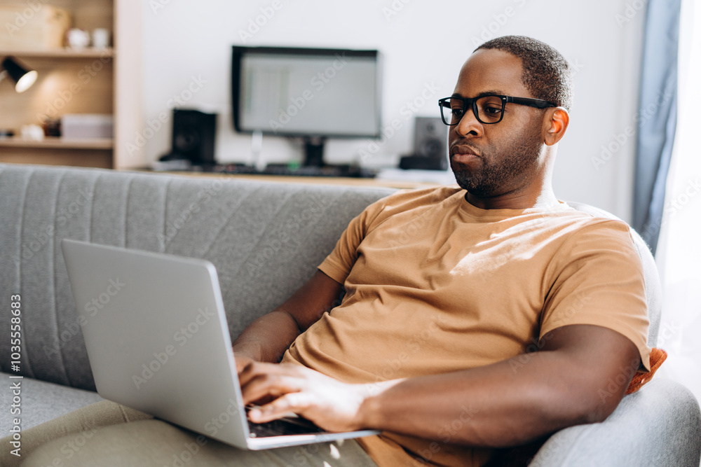 Attentive African American man in eyeglasses typing on laptop working at home online Attentive African American man in eyeglasses typing on laptop working at home online