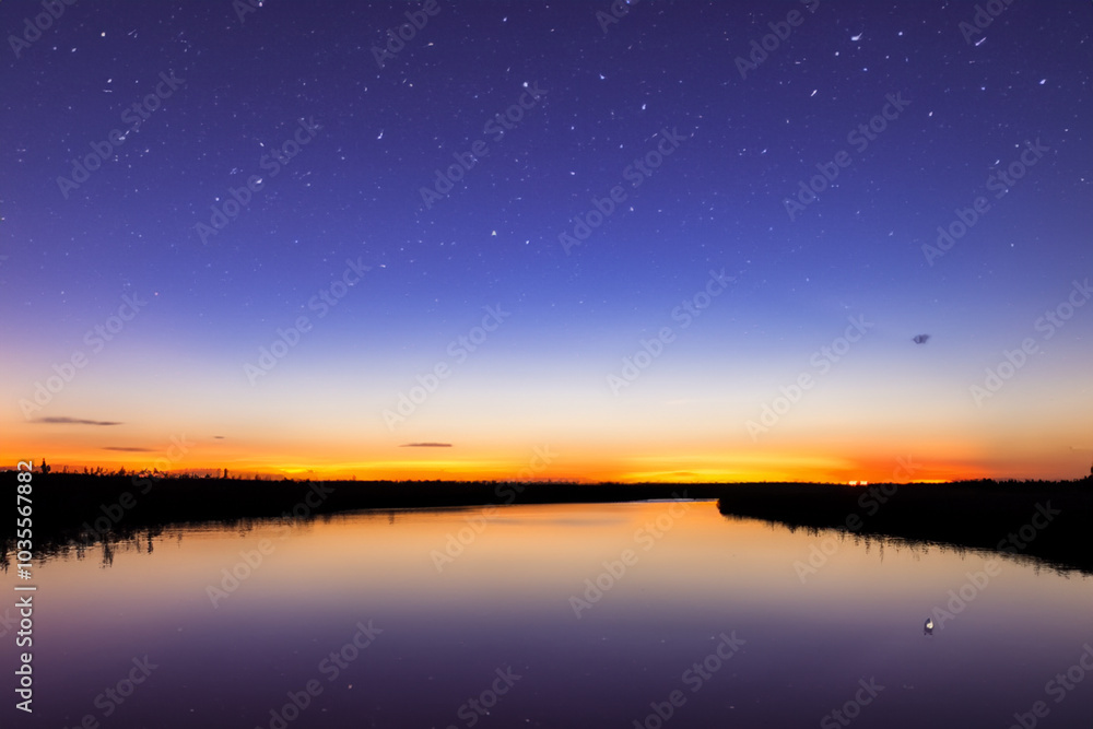 Sunset over river with stars in nature. Landscape sky concept. Dark night with stars and a wide river with forest in the evening. The river flowing through the forest in the evening with dark stars. Sunset over river with stars in nature. Landscape sky concept. Dark night with stars and a wide river with forest in the evening. The river flowing through the forest in the evening with dark stars.