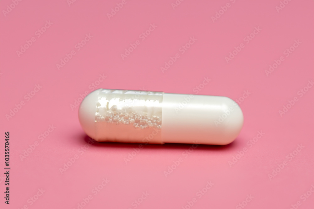Capsule in pink and white on white. health medicine pill concept. small white capsule lying on a pale pink. a small white capsule lies on a pale pink with a blue and medical lifestyle terminology. Capsule in pink and white on white. health medicine pill concept. small white capsule lying on a pale pink. a small white capsule lies on a pale pink with a blue and medical lifestyle terminology.