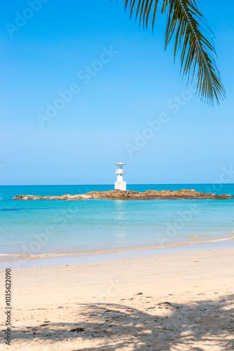 White lighthouse on rocky shoal in sea on tropical coast. Vertical Seascape photo