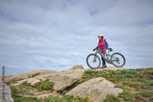 active senior woman cycling with her electric mountain bike at the rocky red granite cost next to Ploumanac'h, Côtes d'Armor,Brittany, France