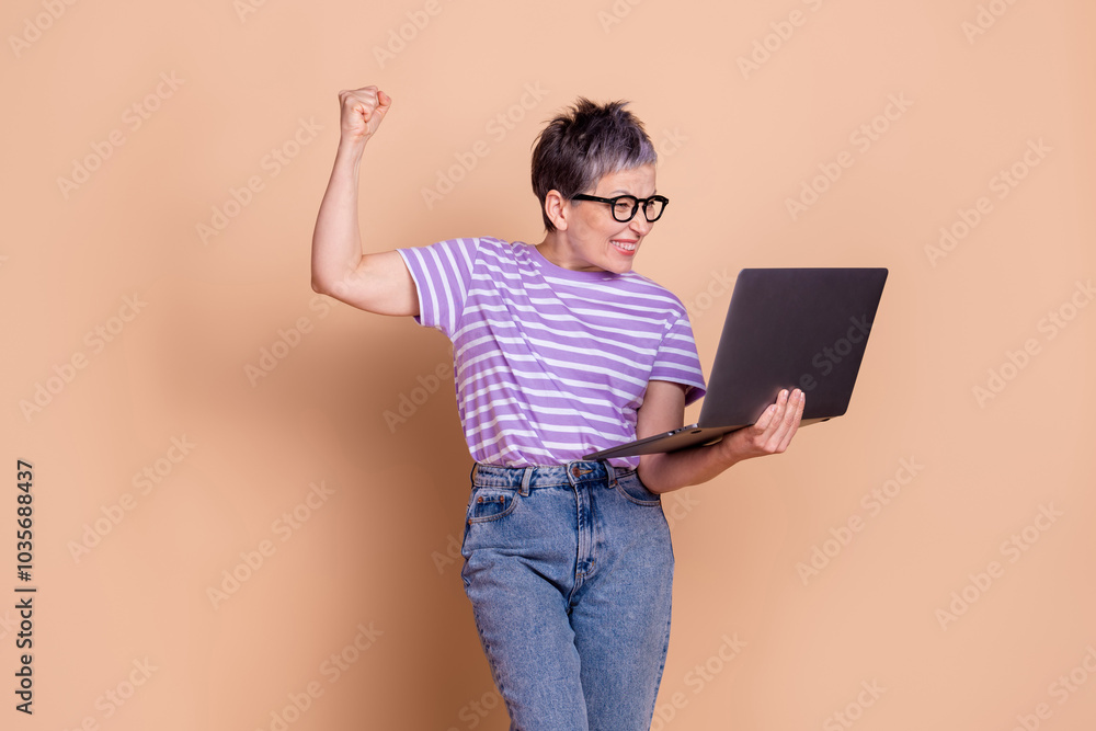 Photo of positive adorable pensioner woman wear stylish clothes raise hand fist isolated on beige color background Photo of positive adorable pensioner woman wear stylish clothes raise hand fist isolated on beige color background