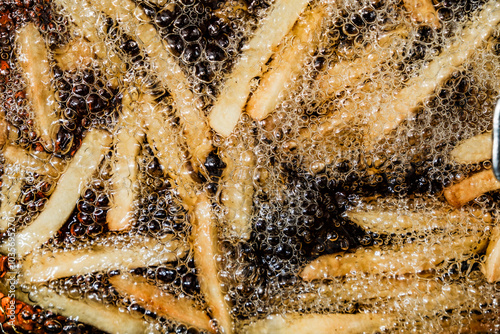 Photography French fries bubbling in hot oil, captured up close as they cook to a crispy texture