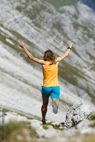 Women Trail runner seen from behind jumping while running with arms in the air