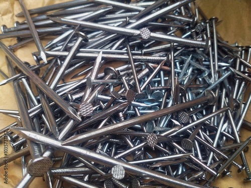 Close-up of a pile of nails on brown paper. This image highlights the clear, shiny smoothness of the new nails, their sharp edges and flat heads, indicating their use in construction and woodworking.