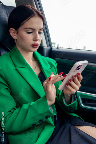 A girl in a green jacket is texting on the phone while driving a car.