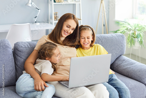 Happy family time, smiling kids, happy mom enjoying leisure at home together, using laptop on sofa, talking on video call, laughing, watching movie, interactive entertainment online TV channel