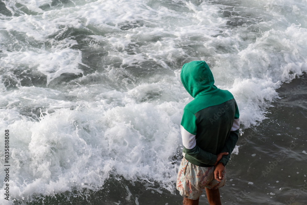 Man with a hood standing on a pier and looking at the Atlantic Ocean. Shorts, sandals. Casablanca, Morocco. Man with a hood standing on a pier and looking at the Atlantic Ocean. Shorts, sandals. Casablanca, Morocco.