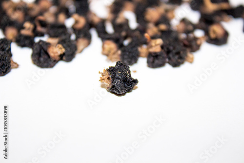 The photo shows dried black currants. These are small, dark, almost black pieces with brown elements, which might be remnants of stems or pedicels. They have a wrinkled texture, typical for dried berr