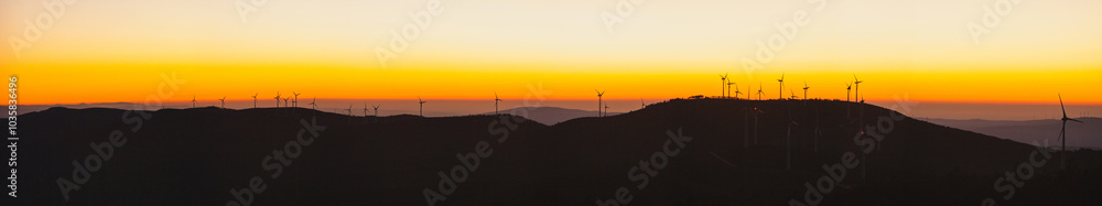 Obraz premium a landscape of wind turbines silhouetted against a vibrant sunset.
