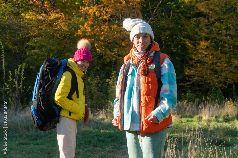 family walking in autumn forest with backpacks, boy in yellow jacket, girl in pink jacket, mother in orange sleeveless jacket, family in hat with pompoms, gen z family walking in autumn forest with backpacks, boy in yellow jacket, girl in pink jacket, mother in orange sleeveless jacket, family in hat with pompoms, gen z