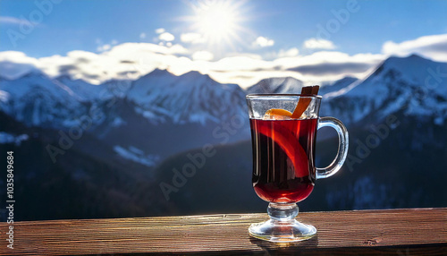 A glass of hot mulled wine stands on the balcony overlooking the snow-capped mountains. A glass of mulled wine stands against the backdrop of high snow-capped mountains. photo