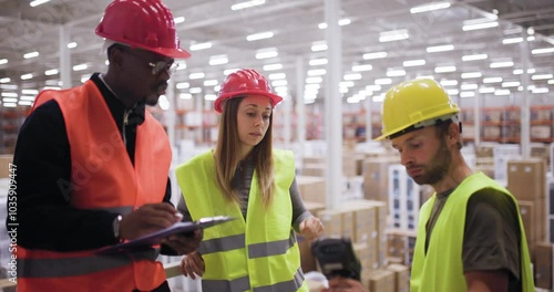 Warehouse workers in safety gear collaborating on logistics tasks with a tablet and scanner in a large industrial storage facility