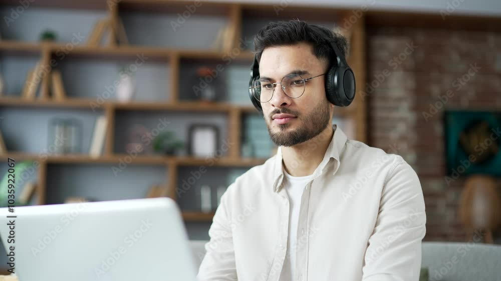 Focused IT specialist in wireless headphones works remotely on a laptop sitting on a sofa in room at home office Serious coder developer is programming, busy with a project on the computer. Close up Focused IT specialist in wireless headphones works remotely on a laptop sitting on a sofa in room at home office Serious coder developer is programming, busy with a project on the computer. Close up