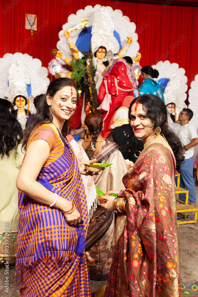 Naklejka premium Two joyful Indian women in traditional sarees performing the Bengali ritual 