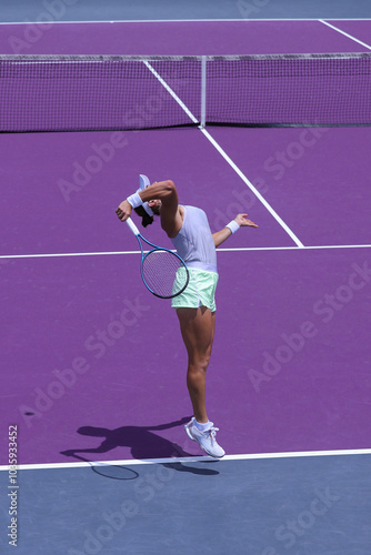 Female tennis player in the air during a jump performing a smash, on a purple clay court