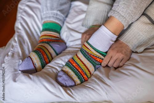 A woman in warm pants putting on a second pair of warm socks to keep warm in the winter without heating, energy and economic crisis concept