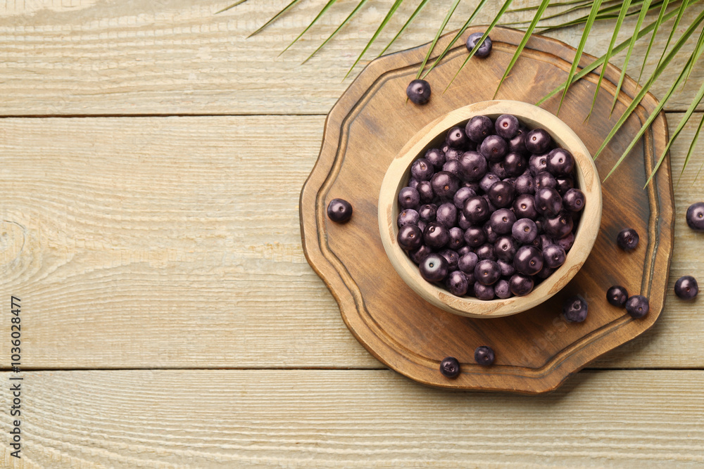 Ripe acai berries in bowl and palm leaves on wooden table, flat lay. Space for text Ripe acai berries in bowl and palm leaves on wooden table, flat lay. Space for text