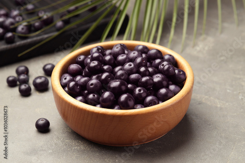 Ripe acai berries in bowl on grey textured table, closeup photo