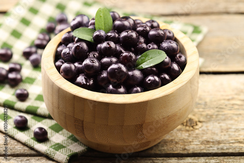 Ripe acai berries and leaves in bowl on wooden table, closeup photo