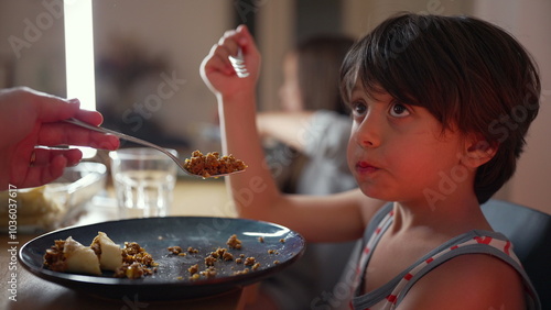 Fotografia Reluctant young boy being fed by a parent, initially hesitating but then opening