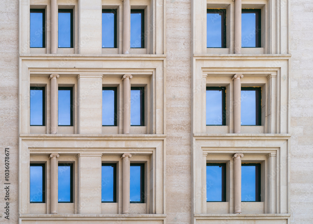 Fototapeta premium Windows of a modern building with blue reflective glass. The facade of the building is lined with light beige natural stone tiles. Contemporary architecture walls with columns. Front view.