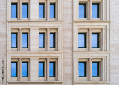 Windows of a modern building with blue reflective glass. The facade of the building is lined with light beige natural stone tiles. Contemporary architecture walls with columns. Front view. photo