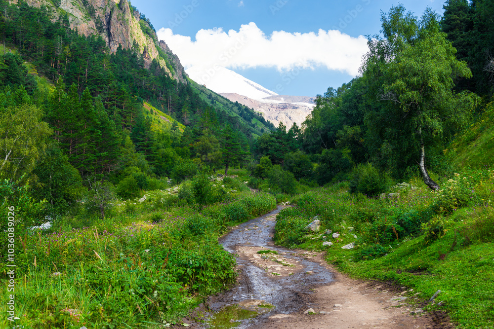 Beautiful mountain landscape with a hiking trail and a view of the snow-capped peak of Elbrus volcano. Caucasus, Elbrus region. Beautiful mountain landscape with a hiking trail and a view of the snow-capped peak of Elbrus volcano. Caucasus, Elbrus region.