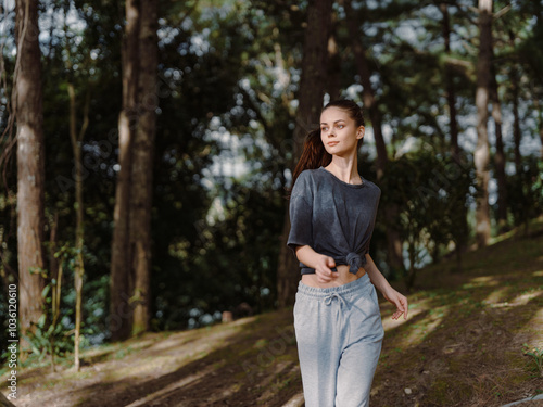 Young woman walking through a serene forest, dressed in casual grey attire, showcasing calm emotions and connecting with nature Peaceful and refreshing atmosphere