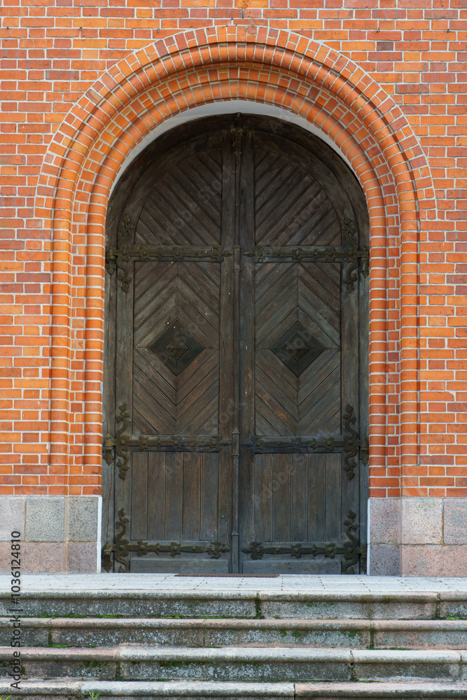 A large wooden church gate in a medieval church. The Gothic building is made of red brick. Decorative elements of the ancient temple. A large wooden church gate in a medieval church. The Gothic building is made of red brick. Decorative elements of the ancient temple.