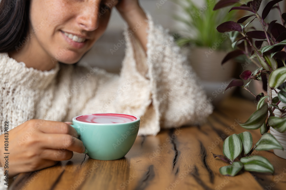 Close-up happy young woman smiling in a cafe holding a cup of matcha tea with raspberry, heart-shaped latte art, cappuccino coffee with red foam and heart, decoration with plants, vegan hot drink Close-up happy young woman smiling in a cafe holding a cup of matcha tea with raspberry, heart-shaped latte art, cappuccino coffee with red foam and heart, decoration with plants, vegan hot drink