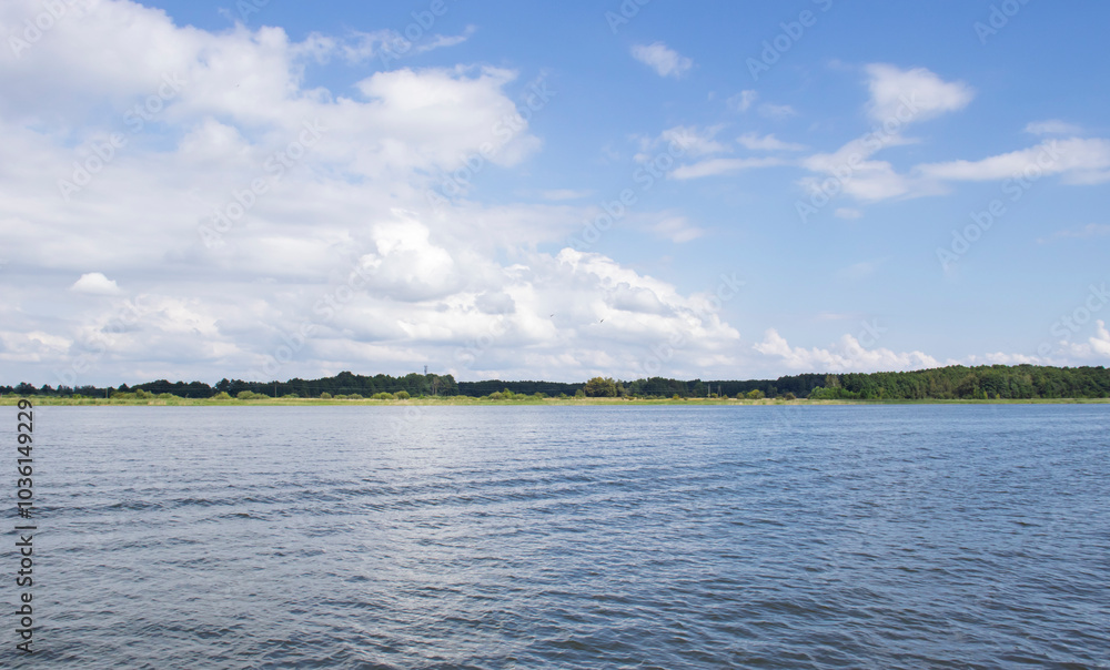 Serene landscape of a calm river surrounded by lush greenery under a beautiful blue sky with fluffy clouds, perfect for nature lovers and outdoor enthusiasts. Serene landscape of a calm river surrounded by lush greenery under a beautiful blue sky with fluffy clouds, perfect for nature lovers and outdoor enthusiasts.