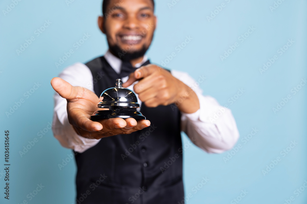 Bellboy personnel using the service bell to provide his services and help the hotel guests, wearing a suit and tie as uniform. Receptionist working at a five star holiday resort, tourism. Bellboy personnel using the service bell to provide his services and help the hotel guests, wearing a suit and tie as uniform. Receptionist working at a five star holiday resort, tourism.
