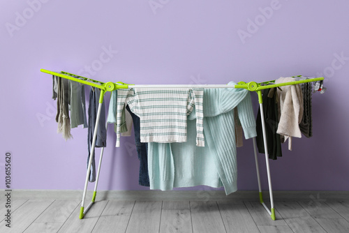 Fotografía Dryer with winter clothes on floor near purple wall