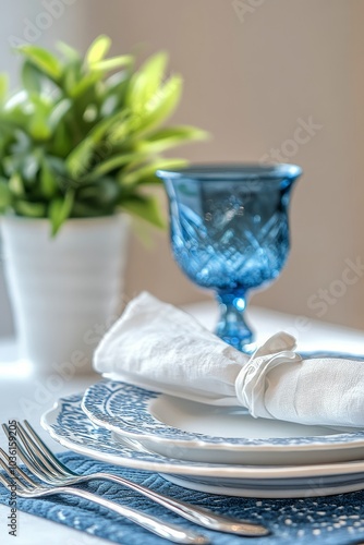 Elegant blue glass on a beautifully set dining table with a green plant by th...